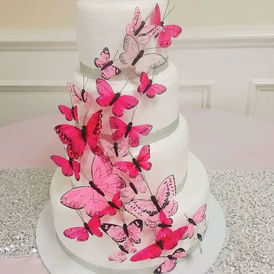 A multi-tiered white cake adorned with numerous pink and fuchsia butterfly decorations.