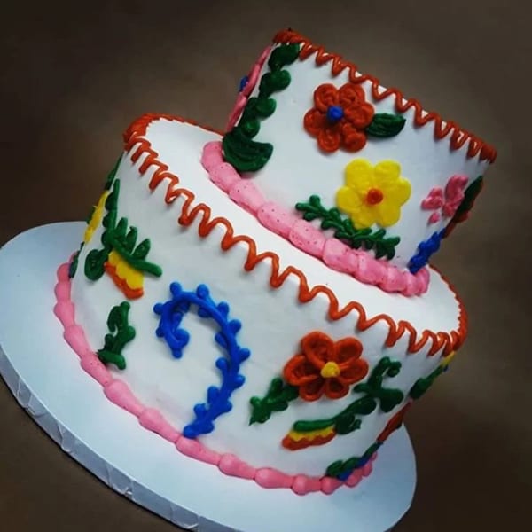 Two-tiered white cake with colorful Mexican folk art floral and scroll designs.