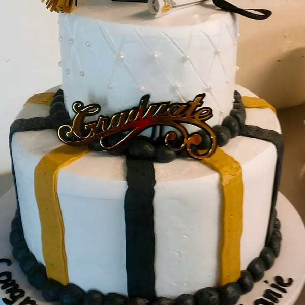 Two-tier white graduation cake with gold and black stripes, a gold "Graduate" topper, and black icing trim.