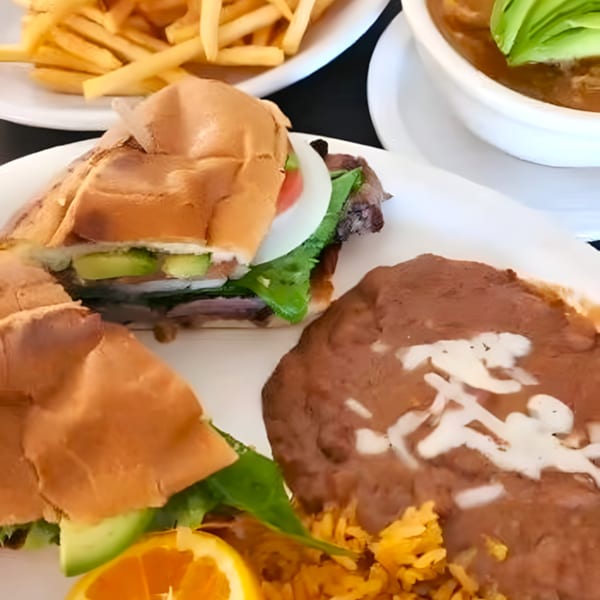 Mexican torta sandwich with avocado, lettuce, and onion, served with refried beans and rice.