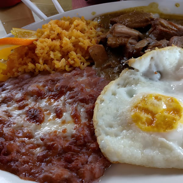 A Mexican breakfast plate with rice, refried beans, chili verde, and a fried egg.