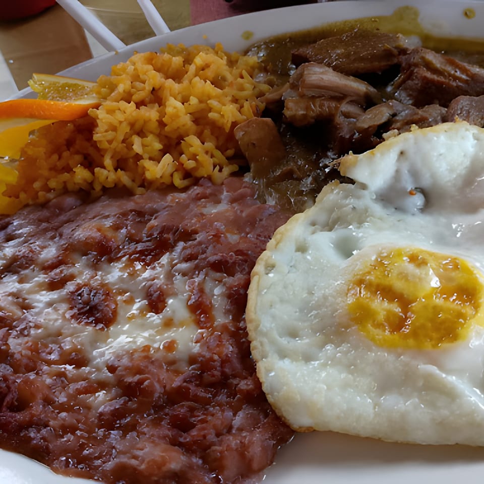 A Mexican breakfast plate with rice, refried beans, chili verde, and a fried egg.
