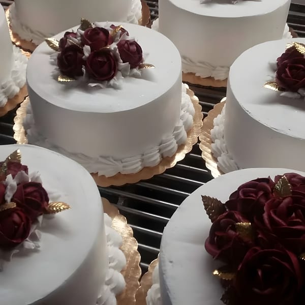 Several white frosted cakes with red rose and gold leaf decorations on golden scalloped bases.