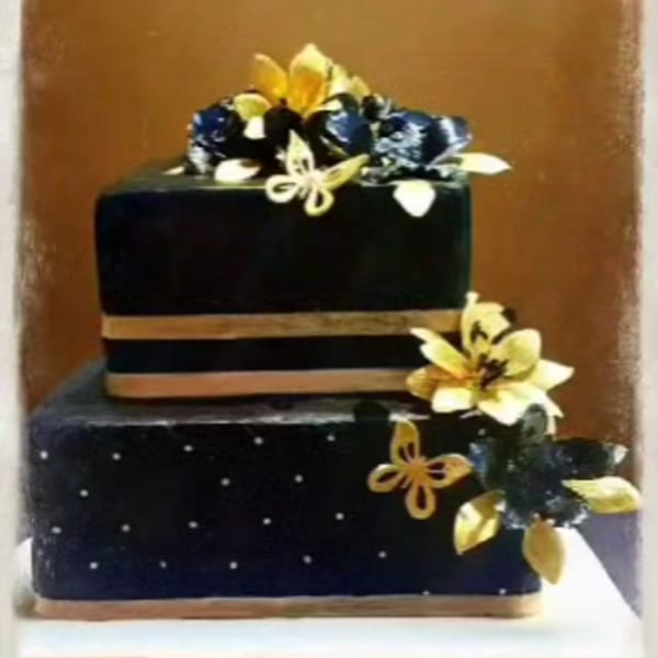 Two-tiered black cake with gold ribbons, white polka dots, and gold and black floral decorations.