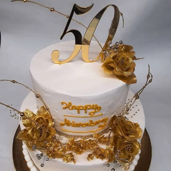 Two-tier white anniversary cake with gold "50" topper, gold flowers, and "Happy Anniversary" script.
